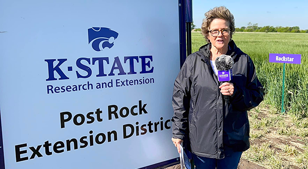 Sandra Wick, Crop Production Agent in the field standing by the Post Rock Extension Plot sign